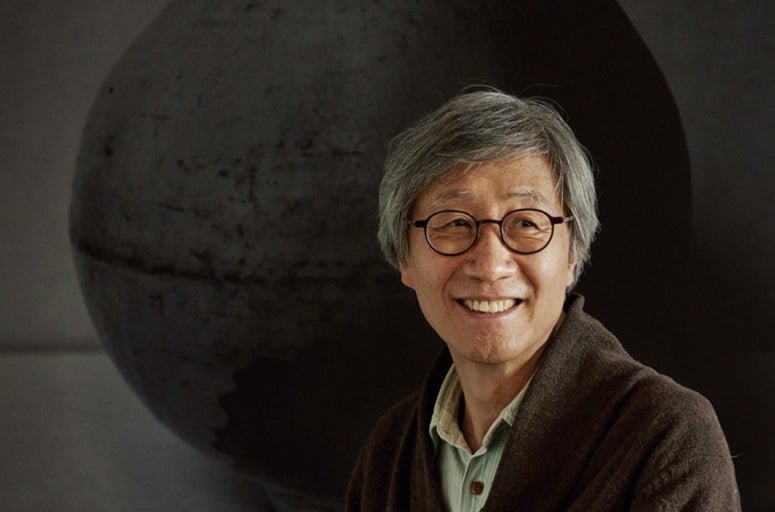 사진가 구본창. 어두운 달항아리를 배경으로 앉아 있다.