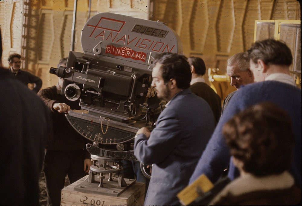 촬영 현장. 나무 상자 위에 놓인 대형 영화 카메라에 PANAVISION SUPER CINERAMA 라고 적혀 있고, 제작진 여러 명이 카메라를 살펴보고 있다.