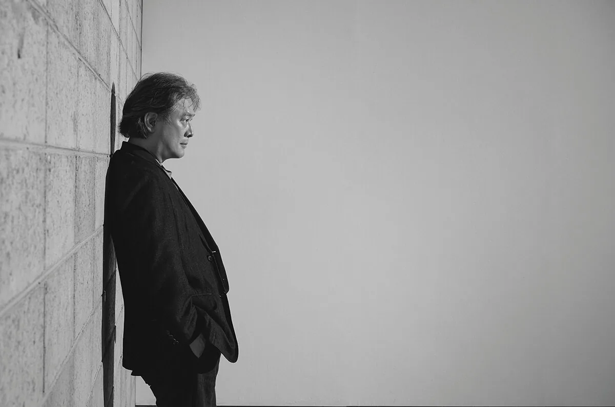 벽에 기대어 옆을 바라보는 박찬욱 감독의 흑백 초상.