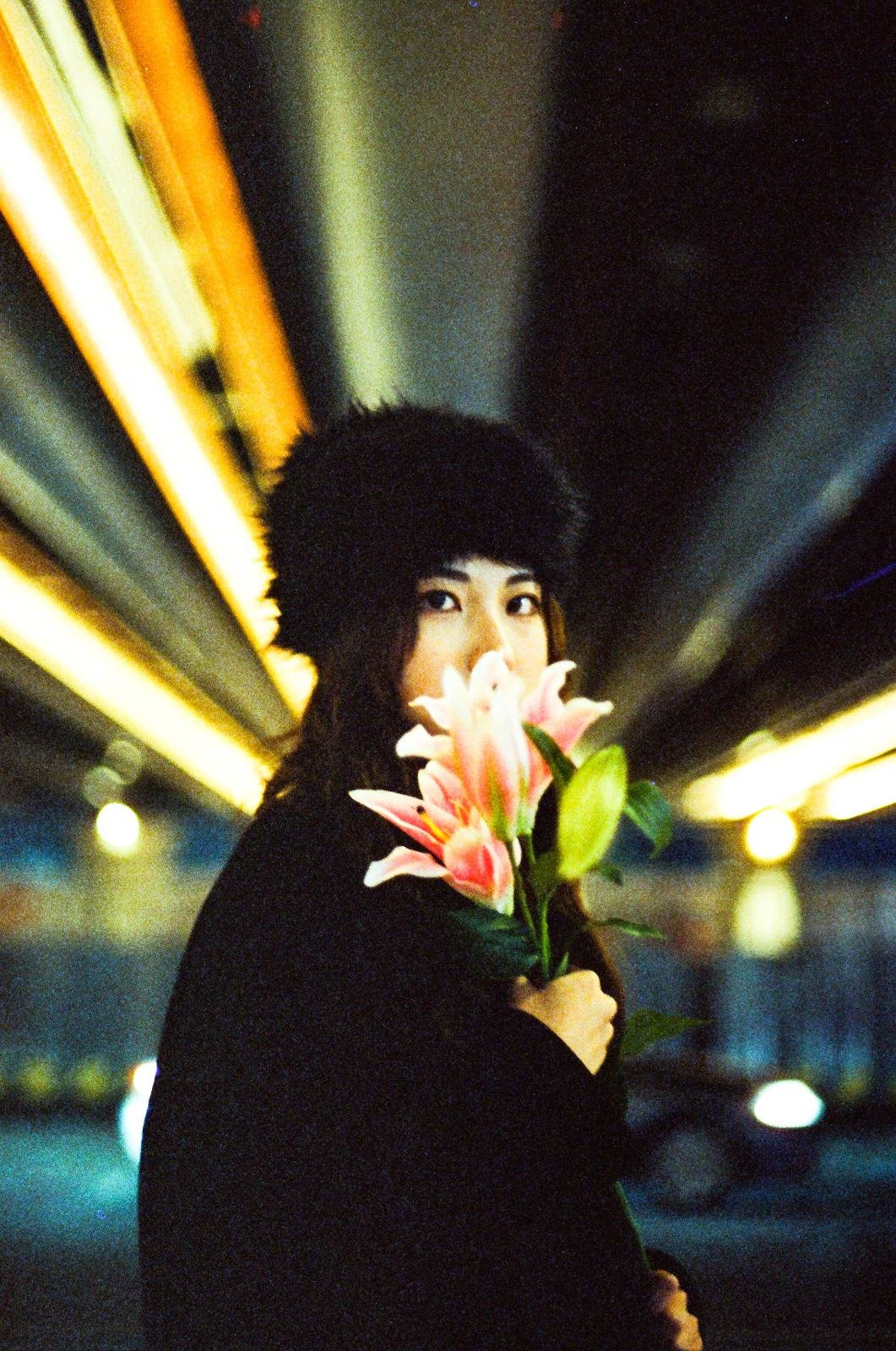明かりの下で花を持ち、黒い帽子をかぶった人。