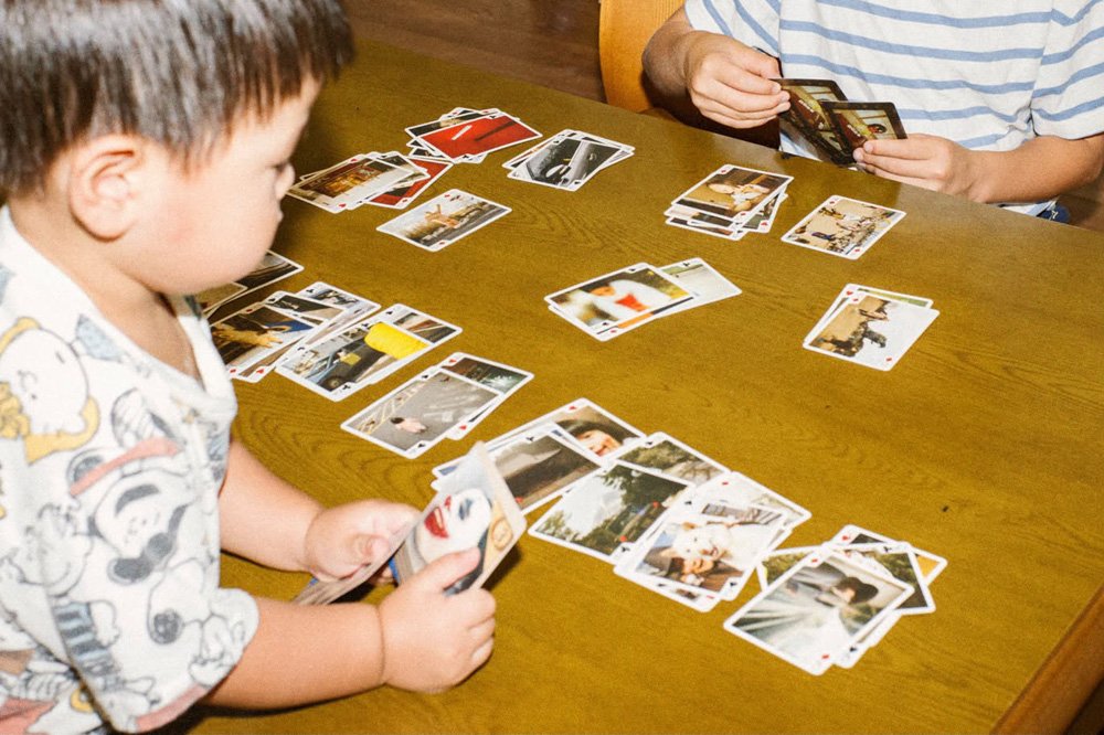 木の食卓にカードを並べ、小さな子どもと大人がトランプで遊んでいる
