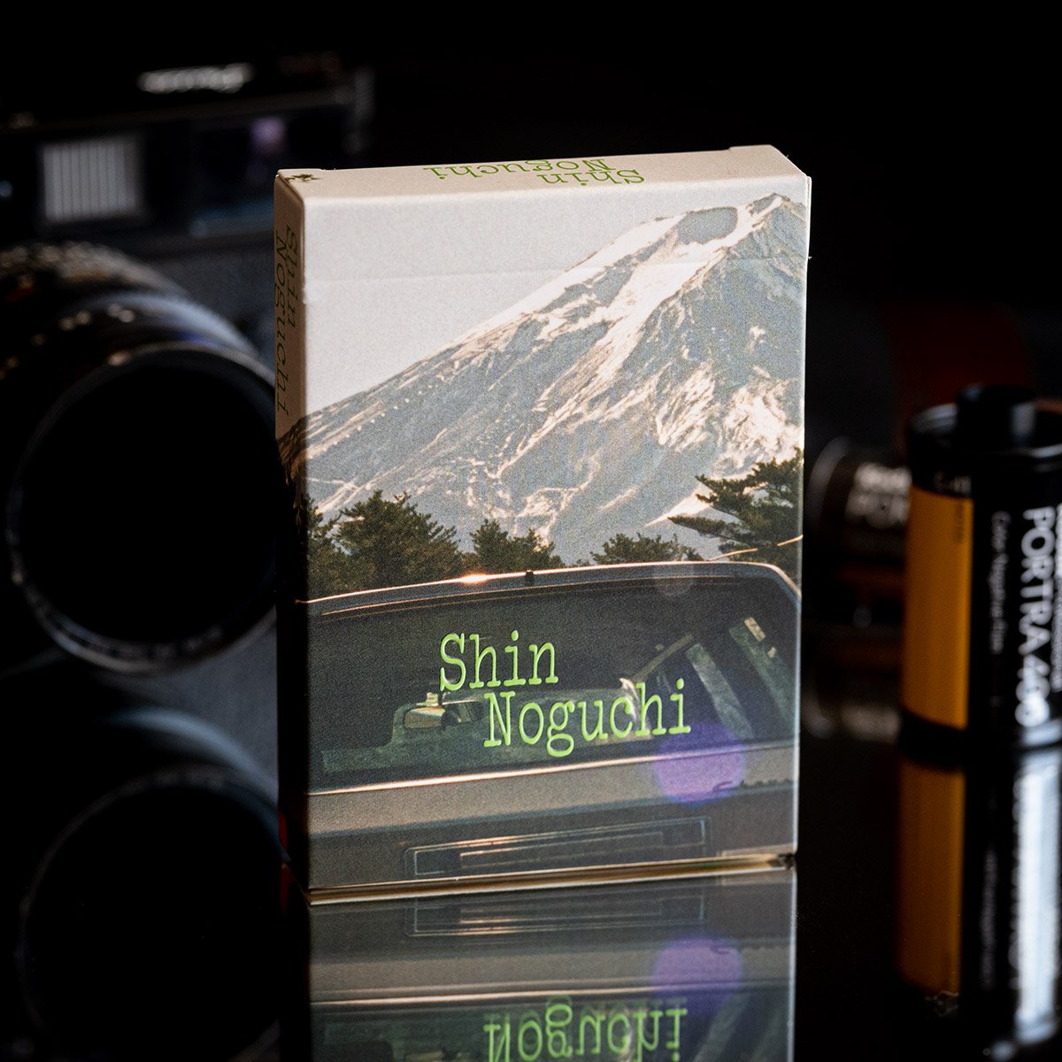 黒い台の上に立つトランプの箱。上に雪をかぶった富士山の写真、下に緑の文字でShin Noguchiとある